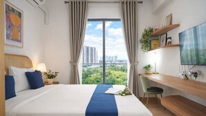 A hotel room with a large bed, a desk, a TV, and a city view. - Studio Japandi Areum Residence At Sky House Bsd (Pagedangan)