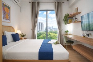Quarto de hotel com uma cama grande, uma escrivaninha, televisão e vista para a cidade.