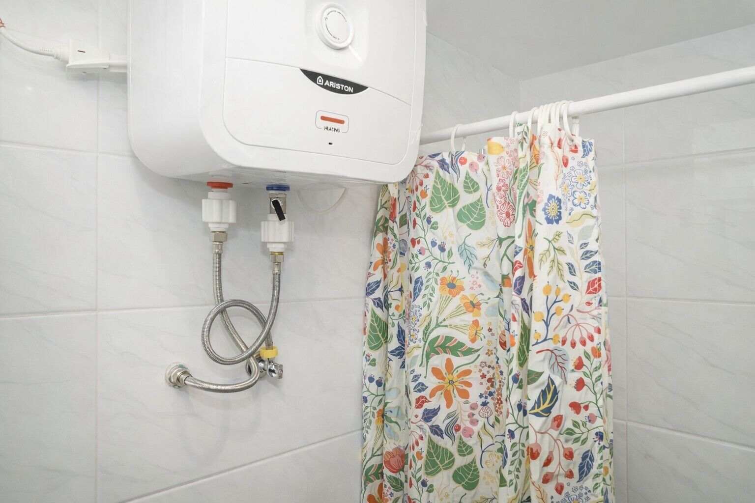 A bathroom with a white showerhead, a colorful floral shower curtain, and a white tiled wall.