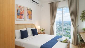 A hotel room with a bed, a nightstand, a lamp, a window with curtains, and two framed artworks on the wall.