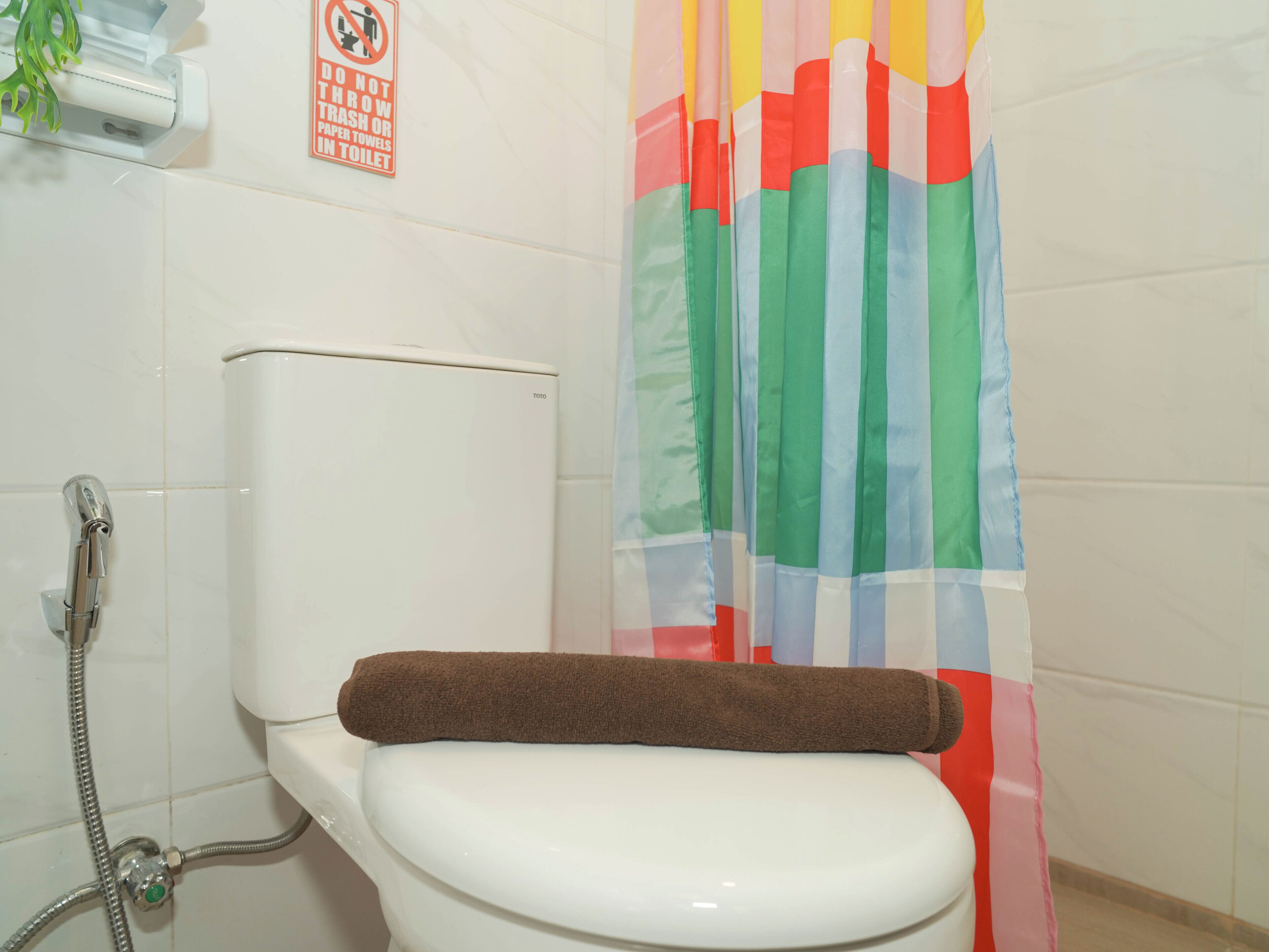 Un baño con inodoro blanco, cabezal de ducha y cortina de ducha a rayas coloridas.