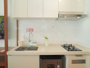 A kitchen with white cabinets, a stainless steel range hood, a sink with a faucet, a dish rack, a small potted plant, and a dishwasher. - Studio Metropolitan Areum Residence At Sky House Bsd (Balaraja)