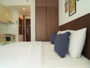A hotel room with a bed, a wooden wardrobe, a kitchenette, and a framed picture on the wall. - Studio Metropolitan Areum Residence At Sky House Bsd (Balaraja)