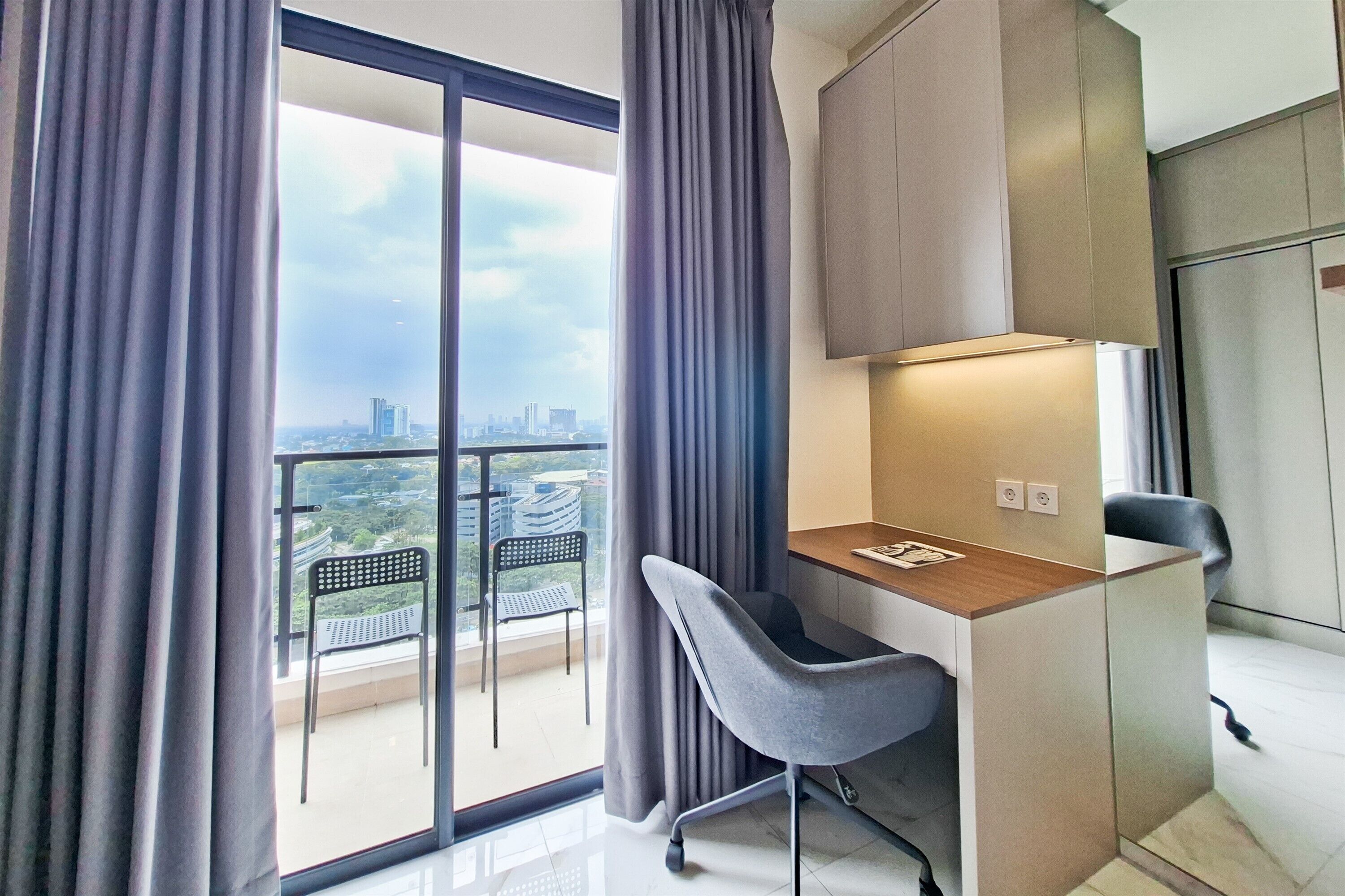 Ein modernes Zimmer mit Schreibtisch, Stuhl und großer Glasschiebetür, die auf einen Balkon führt.