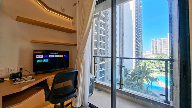 Ein modernes Zimmer mit Fernseher, der Netflix zeigt, einem Schreibtisch mit Stuhl und einem großen Fenster mit Blick auf Hochhäuser und einen Pool.