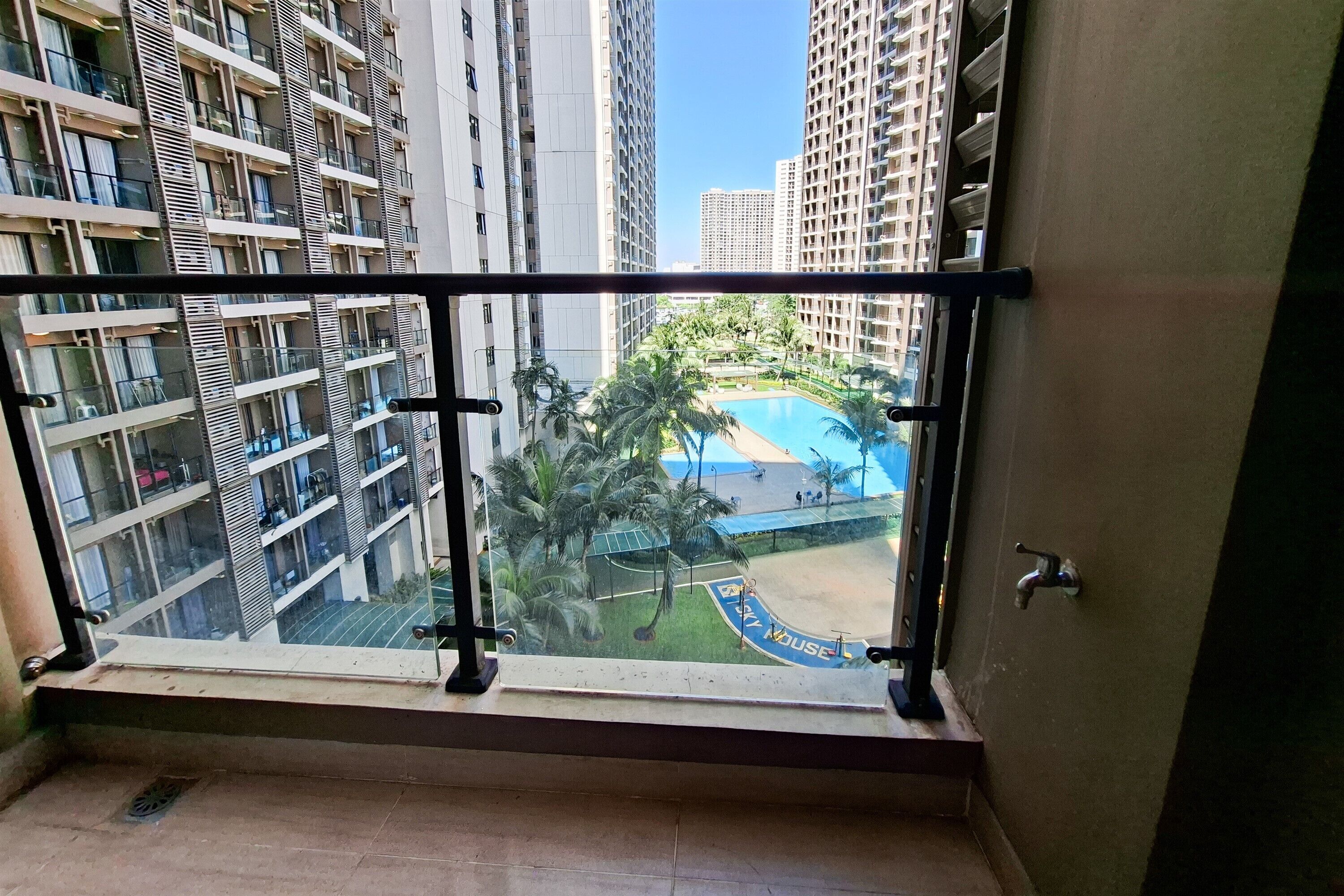 Un balcón con vistas a edificios altos, una piscina y una cancha de tenis.
