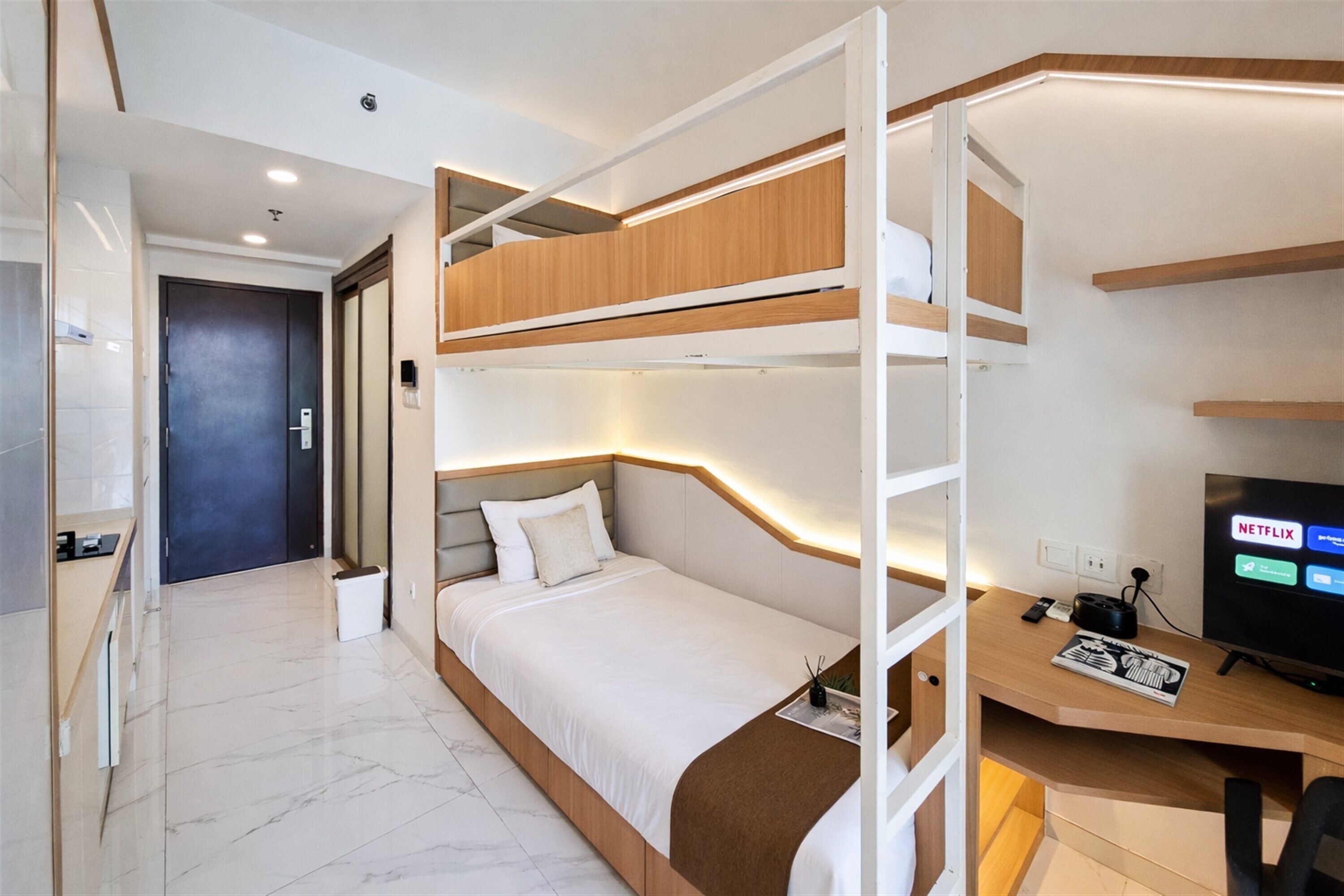 A bunk bed with a desk and a TV, a bathroom with a toilet and sink, and a door to another room.