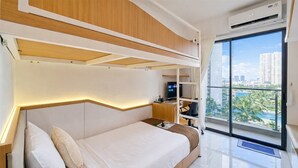Ein modernes Schlafzimmer mit Bett, Einbauschränken, Fernseher und einem Balkon mit Blick auf die Stadt.