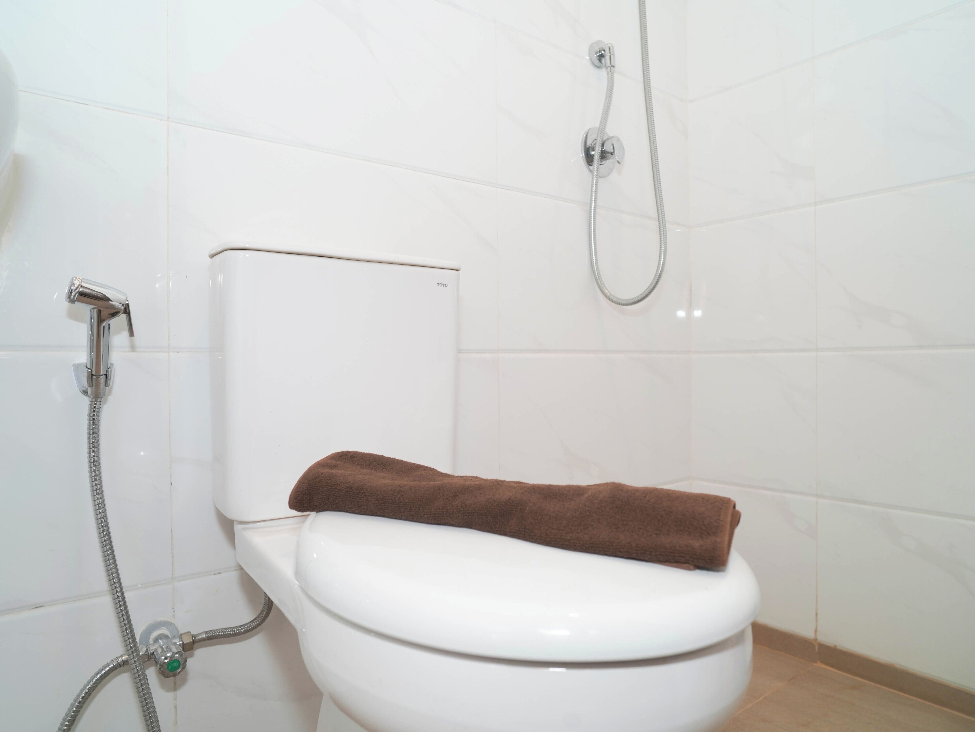 Eine weiße Toilette mit einem braunen Handtuch darauf, einer Duschbrause und einem Toilettenpapierhalter.