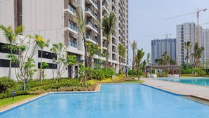 A modern building with a swimming pool, surrounded by greenery and palm trees. - Bright And Homey Studio Room At Apartment Sky House Bsd (Balaraja)