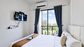 Ein Hotelzimmer mit Bett, einem an der Wand befestigten Fernseher und einem Fenster mit Vorhängen.