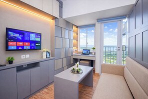 A modern living room with a flat-screen TV, a laptop on a desk, a sofa, and a balcony with a view. - Studio Chic Areum Residence At Tokyo Riverside (Teluknaga)