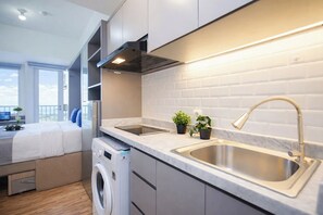 A modern kitchen with a built-in washing machine, a large sink, and a view of the balcony. - Studio Chic Areum Residence At Tokyo Riverside (Teluknaga)