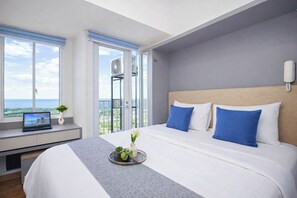 A modern hotel room with a large bed, a laptop on a desk, a balcony with a view, and a phone on the wall. - Studio Chic Areum Residence At Tokyo Riverside (Teluknaga)