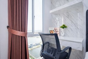 A modern office chair, a white shelf with a vase and a poster, and a view of a river through a window. - Cozy And Neat Studio At Apartment Tokyo Riverside Pik 2 (Teluknaga)