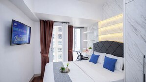 Ett hotellrum med en säng, en TV, ett skrivbord och utsikt över byggnader.