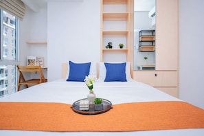 A hotel room with a bed, a desk, a chair, a shelf with plants, and a window. - Practical Studio Near Tokyo Hub At Tokyo Riverside Pik 2 Apartment (Teluknaga)