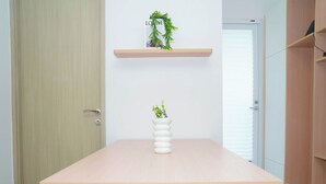 Egy letisztult, minimalista szoba, melyben egy fa asztal, egy fekete szék, egy fehér vázában elhelyezett növény és egy fa polcon szintén egy növény található.