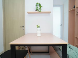 Pelkistetty huone, jossa on puinen pöytä, musta tuoli, valkoinen maljakko, jossa on kasvi, ja puinen hylly, jossa on myös kasvi.