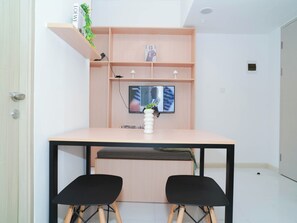 Ein modernes Zimmer mit einem Holztisch, zwei schwarzen Stühlen, einem an der Wand befestigten Fernseher und einer kleinen Ablage mit Dekorationen.