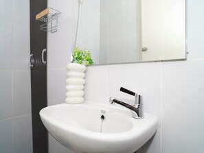 A white bathroom sink with a chrome faucet, a mirror above it, and a small plant on the wall. - Chic Green Studio Room At Apartment Tokyo Riverside Pik 2 (Teluknaga)