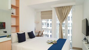 Ein Hotelzimmer mit Bett, Schreibtisch, Stuhl, Fernseher und einem Fenster mit Vorhängen.
