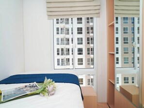 A bedroom with a bed, a window with a view of a building, and a wooden wardrobe. - Stylish And Functional 2Br Apartment At Tokyo Riverside Pik 2 (Teluknaga)