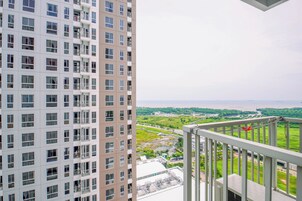 A high-rise building with multiple balconies, a view of a green landscape, and a body of water in the distance.