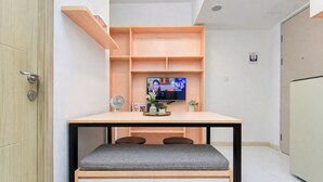Una habitación pequeña con una mesa de madera, una banca, un televisor y un ventilador.