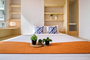 Un dormitorio con una cama, dos plantas en macetas, un estante de madera con adornos y un ventanal con vistas.