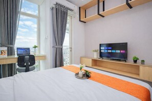 Ein Hotelzimmer mit einem Bett, einem Schreibtisch mit Computer, einem Fernseher und einem Fenster mit Vorhängen.