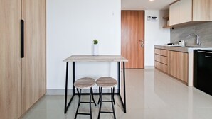 A modern kitchen with a wooden table, two stools, a small potted plant, and a built-in dishwasher. - Comfy And Relaxing Living In Studio At Apartment Cisauk Point (Cisauk)