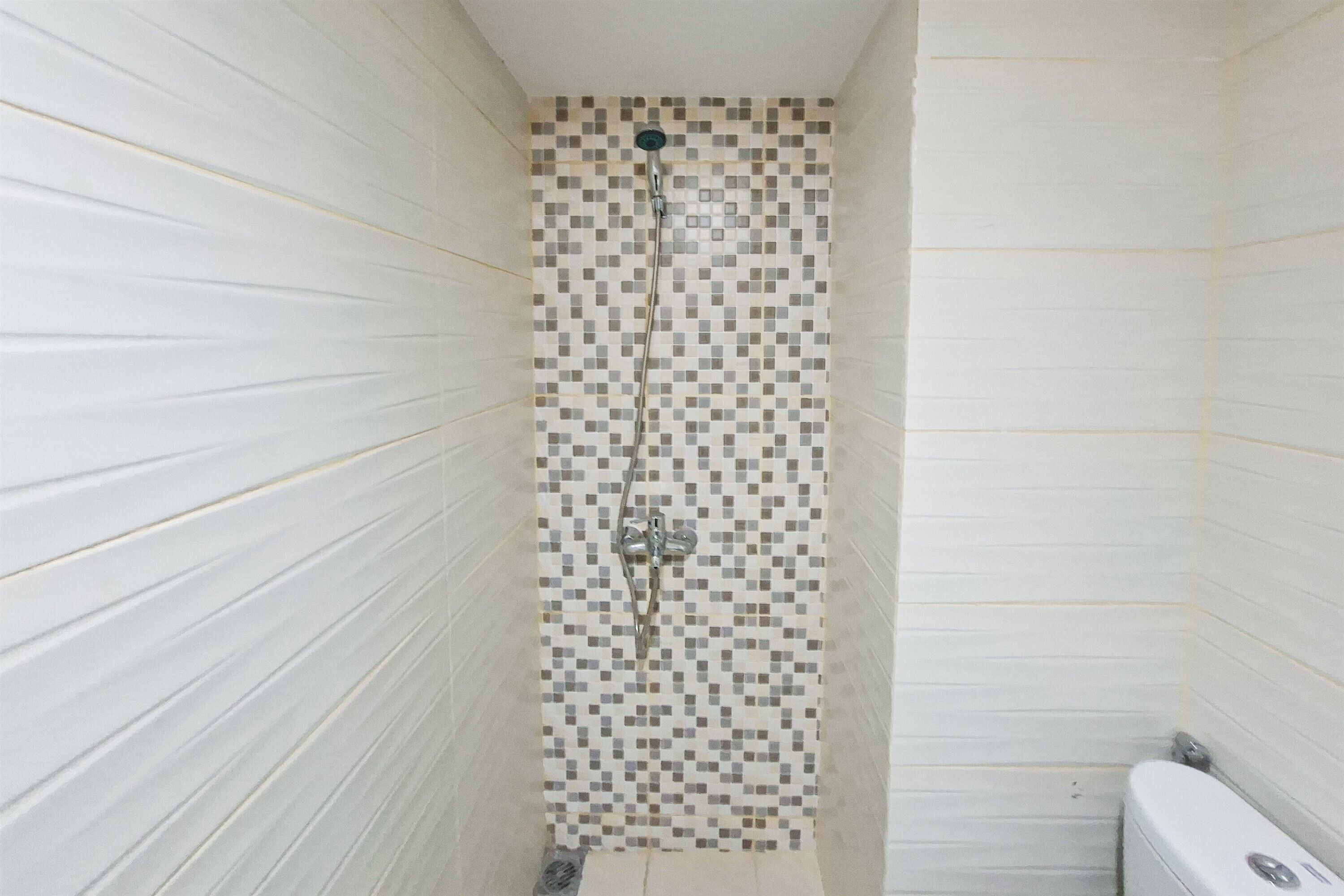 A narrow bathroom with tiled walls, a shower, and a toilet.