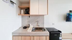 A compact kitchen with a sink, a coffee maker, a refrigerator, and a TV mounted on the wall. - Comfy And Relaxing Living In Studio At Apartment Cisauk Point (Cisauk)