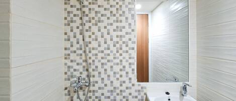 Un baño con pared de ducha azulejada, un lavabo y un espejo.