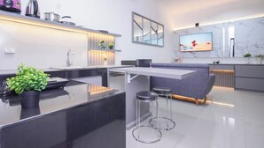 A modern kitchen with a central island, bar stools, a flat-screen TV, and a marble backsplash. - Homey And Modern 2Br At Apartment Green Royal Condo House (Jakarta)