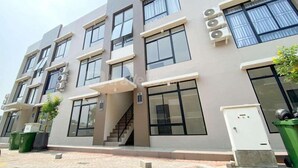 A multi-story building with large windows, a staircase, and outdoor trash bins. - Homey And Modern 2Br At Apartment Green Royal Condo House (Jakarta)