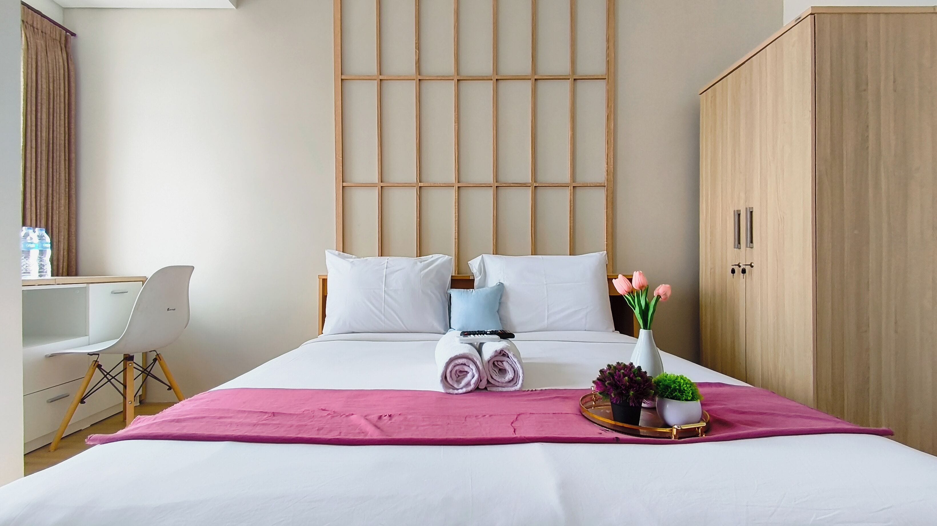 Een hotelkamer met een bed, een bureau, een stoel, een kledingkast en een dienblad met bloemen.