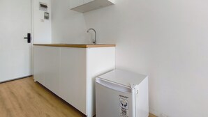 A kitchenette with a white refrigerator, a wooden countertop, and a wall-mounted sink. - Studio Minimalist And Relaxing At Kyo Society Apartment (Surabaya)