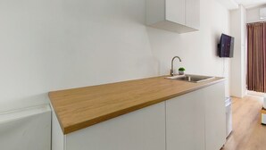 A kitchen with a wooden countertop, white cabinets, a stainless steel sink, and a small potted plant. - Studio Minimalist And Relaxing At Kyo Society Apartment (Surabaya)
