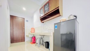 A compact kitchen with a refrigerator, a sink, a countertop, and a wooden cabinet above. - Functional And Cozy Studio At Skyview Medan Apartment (Medan)