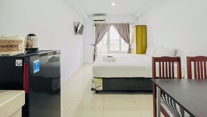 A hotel room with a bed, a desk, a refrigerator, a TV, and a window with curtains. - Functional And Cozy Studio At Skyview Medan Apartment (Medan)