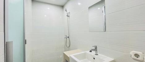 A modern bathroom with white tiles, a sink, a mirror, and a shower.
