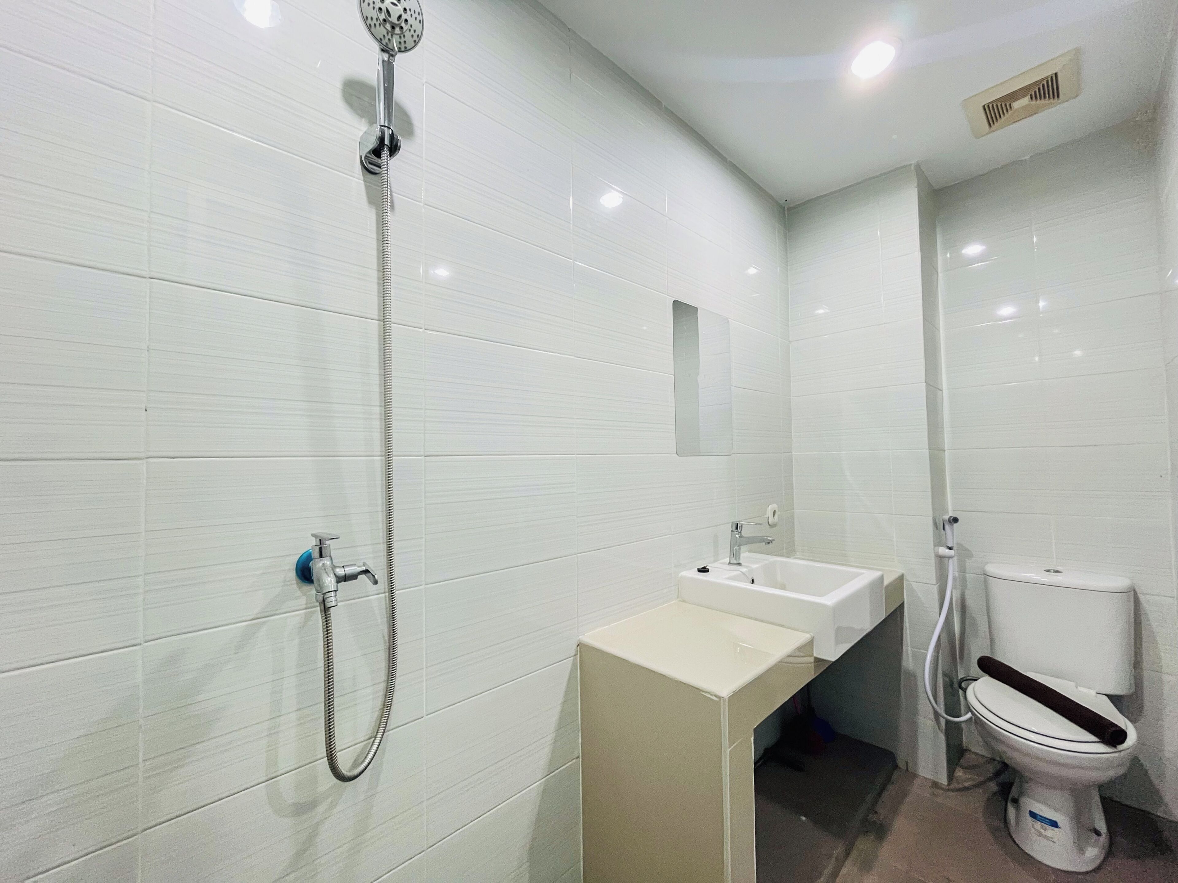 A bathroom with white tiled walls, a shower, a sink, and a toilet.