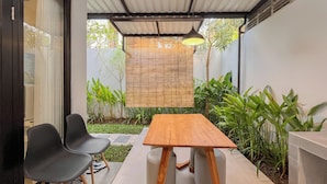 A patio with a wooden table and black chairs, surrounded by greenery and a bamboo screen. - Damara 2BR Villa Jimbaran Near GWK (Jimbaran)