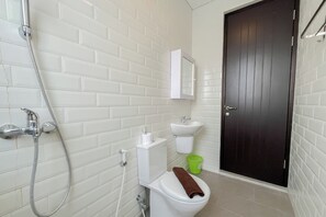 A bathroom with white tiled walls, a black door, a white toilet, a green trash bin, and a white sink. - Cozy Stay 2Br Villa Damara Jimbaran Hijau (Jimbaran)