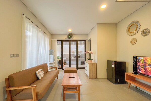 A living room with a sofa, a wooden table, a television, and a refrigerator. - Cozy Stay 2Br Villa Damara Jimbaran Hijau (Jimbaran)