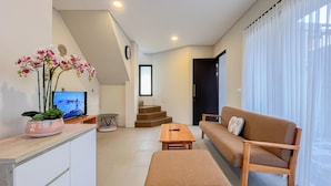 A modern living room with a sofa, ottoman, and a TV on a stand. - Damara 2BR Villa Jimbaran Near GWK (Jimbaran)