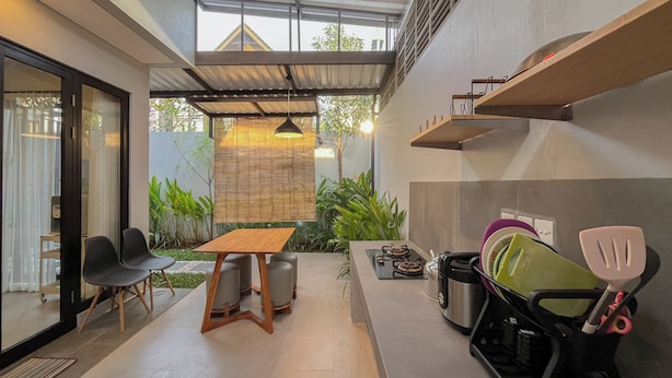 A compact kitchen with a gas stove, a sink, and a dish rack. There is a dining area with a table and chairs. - Damara 2BR Villa Jimbaran Near GWK (Jimbaran)