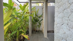 A covered outdoor area with stone walls, large green plants, and a tiled floor. - Damara 2BR Villa Jimbaran Near GWK (Jimbaran)